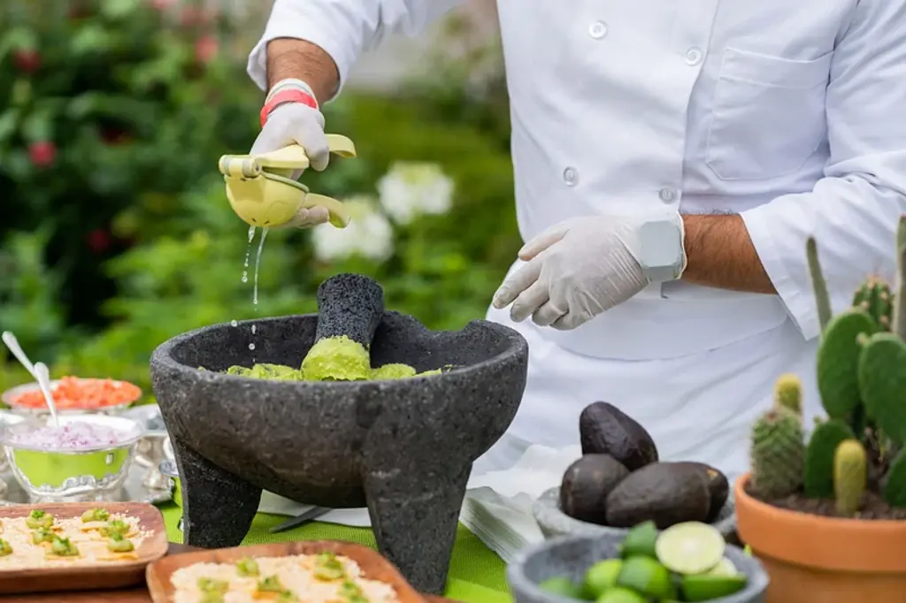 someone making guac in a stone mortar and sqeezing lime juice into it
