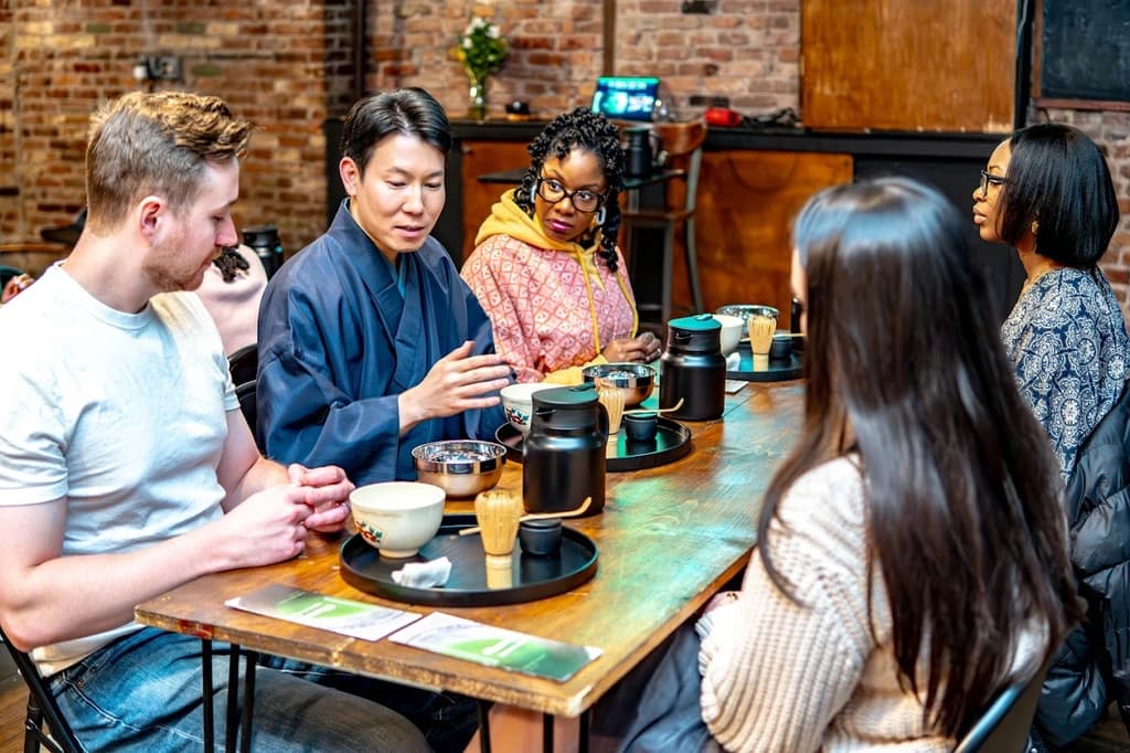 Instructor in traditional attire guiding a small group through a tea ceremony, with participants attentively following the process.