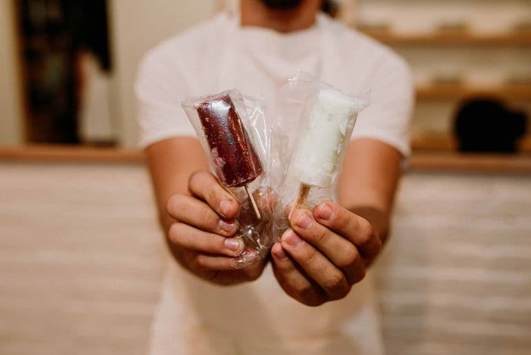 Person holding two individually wrapped mini paletas, showing the small handheld frozen treats served at the cart.