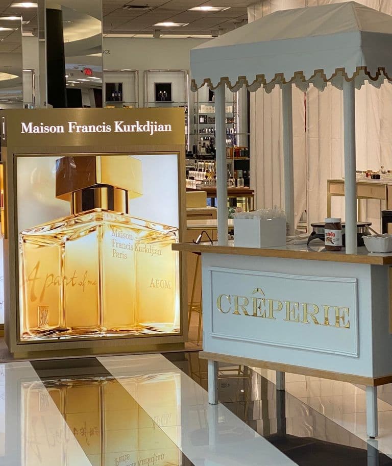A beautifully designed crepe cart labeled "Crêperie," set up in a luxury retail space near a Maison Francis Kurkdjian display.