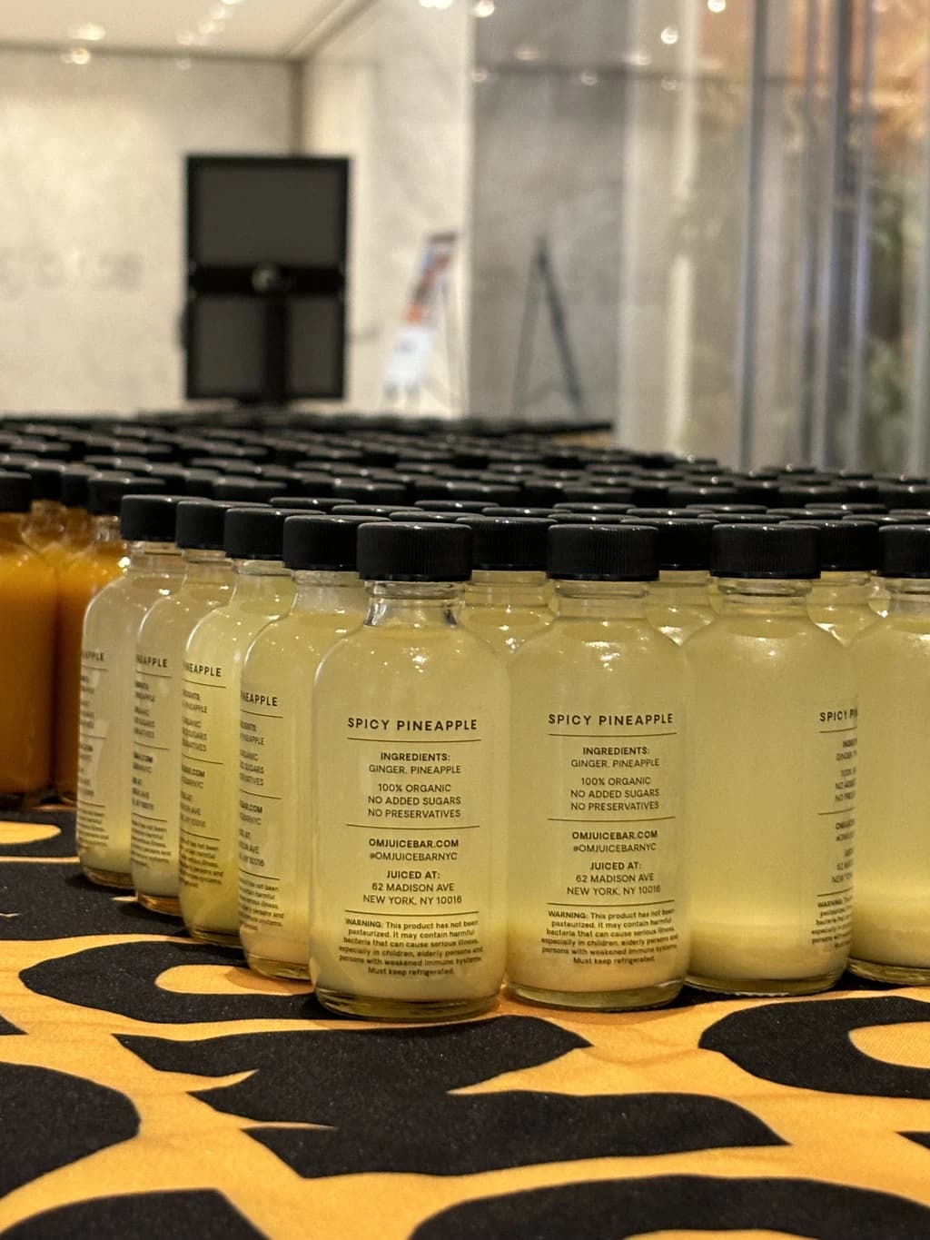 Close-up of 'Spicy Pineapple' wellness shot bottles on a table, showcasing the natural and organic ingredients on the label.